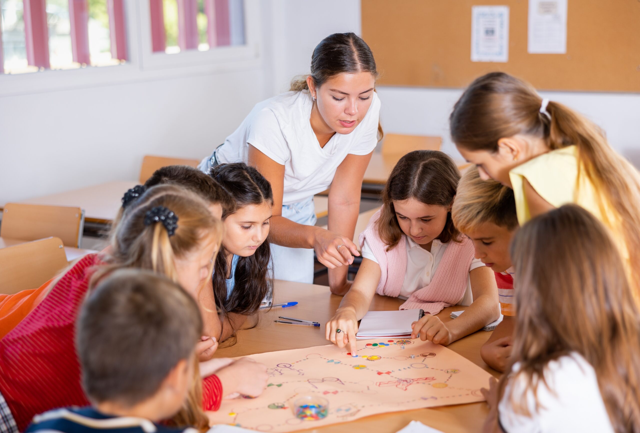 Happy Preteen Children And Female Teacher Playing Together Educational Board Happy Preteen Children And Female Teacher Playing Together Educational Board